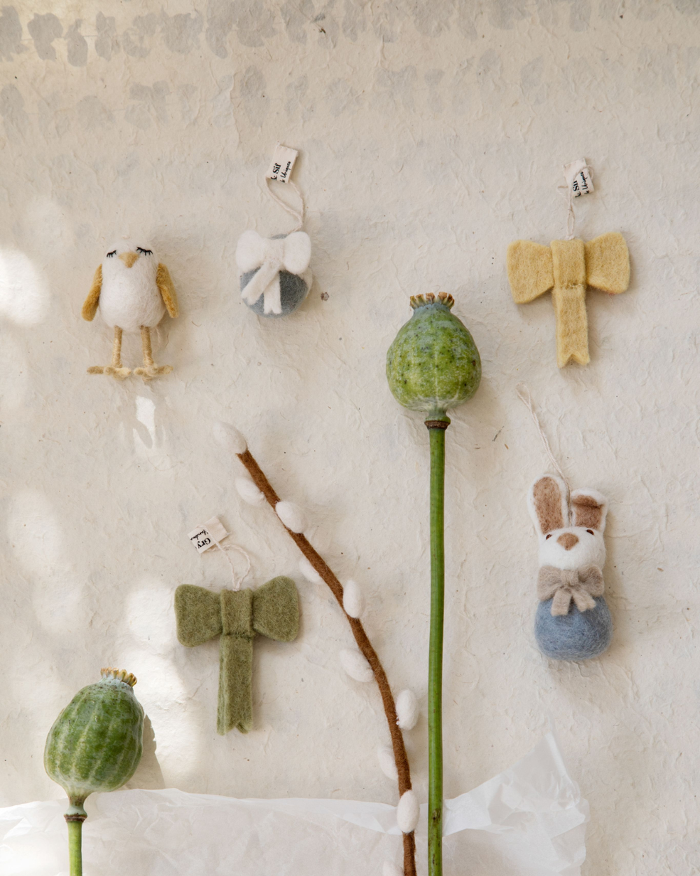 Mehrere Filzanhänger von Gry & Sif, darunter Hasen mit Schleife, Vogel und Zweige, dekorativ arrangiert an einer hellen Wand mit Naturmaterialien.
