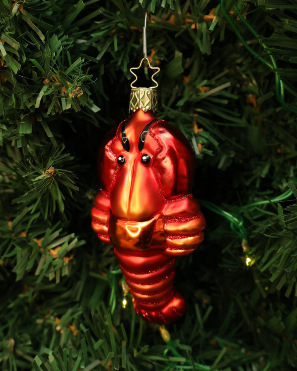 Handgefertigter Hummer Weihnachtsbaumschmuck von Inge Glas. Rot-Orangefarbener Hummer mit schwarzen Fühlern und Glitzer Highlights an einer grünen Tanne befestigt.