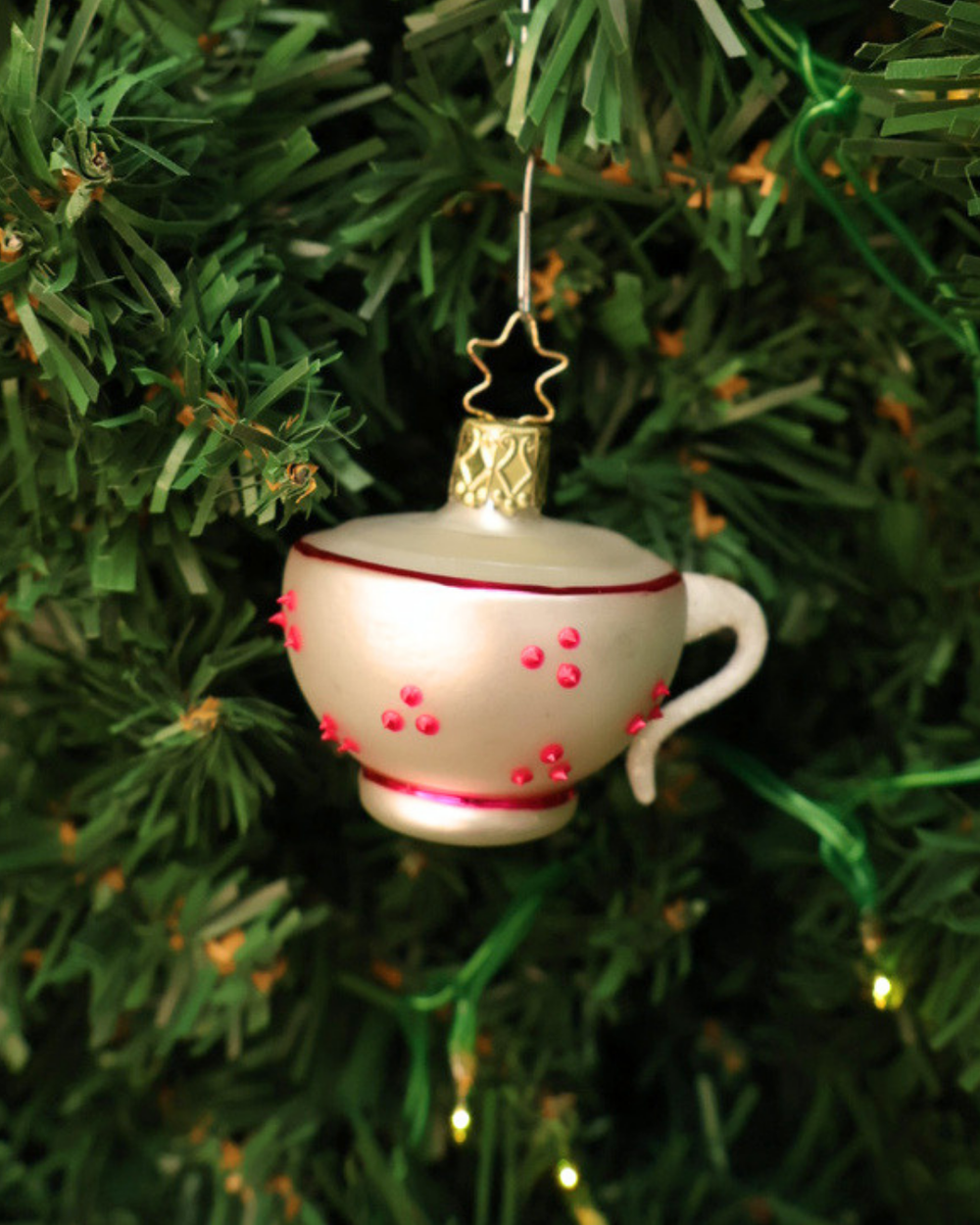 Alice im Wunderland "Kaffeetasse" zum Aufhängen in Deutschland handgefertigt von Inge Glas. Zu sehen ist eine weiße Tasse mit weißem Henkel, roten Punkten und rosa Zierinien am oberen und unteren Tassenrand. Hier aufgehängt an einem Tannenbaum.