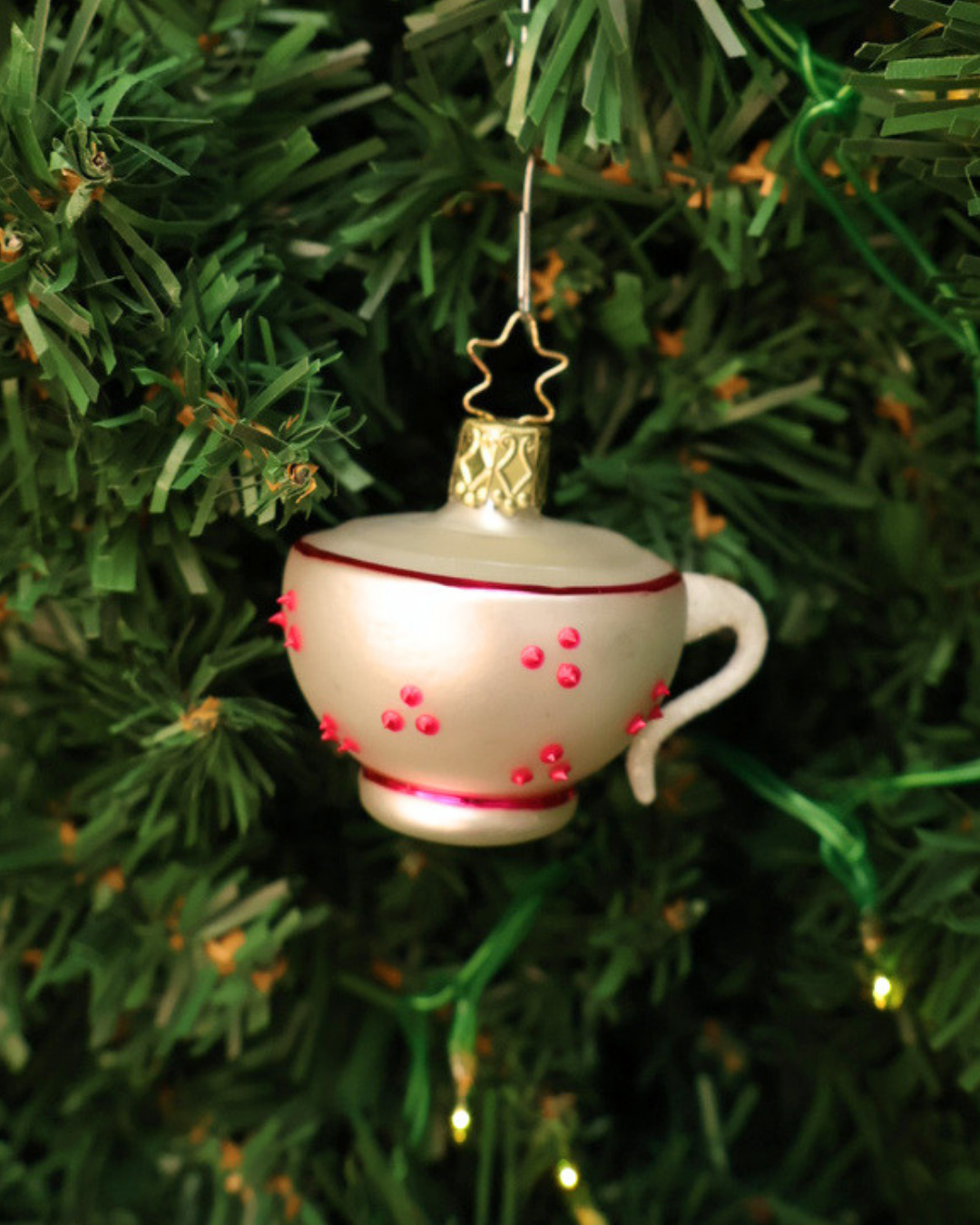 Alice im Wunderland "Kaffeetasse" zum Aufhängen in Deutschland handgefertigt von Inge Glas. Zu sehen ist eine weiße Tasse mit weißem Henkel, roten Punkten und rosa Zierinien am oberen und unteren Tassenrand. Hier aufgehängt an einem Tannenbaum.