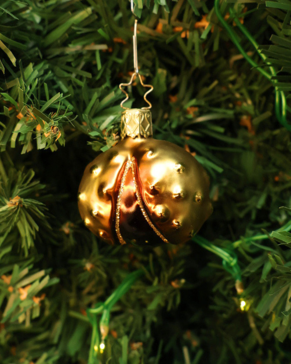 Handgefertigter, in Deutschland hergestellter Kastanienanhänger von Inge Glas mit goldener Kastanienschale und maronenbrauner Kastanie. Hier an einem Kunsttannenbaum hängend.