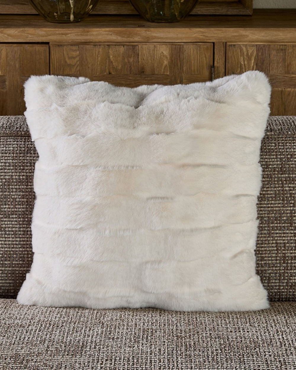 Dekorierter Romolo Faux Fur Kissenbezug auf braun-grauem Sofa.