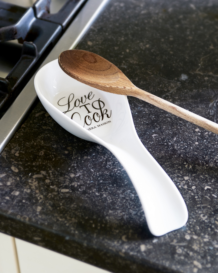 Kochlöffelhalter „Love to Cook“ von Rivièra Maison mit Holzkochlöffel dekoriert auf einer dunklen Küchenarbeitsfläche.