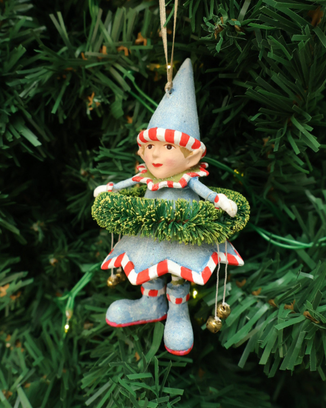 "Dashers Elf" Krinkles von Patience Brewster hängt an Tannenbaum. Zu sehen ist ein Elf mit hellblauen Kleid, Hut, Schuhen und grünen Pflanzen Details. Der Elf hält 2 Glocken in den Händen.