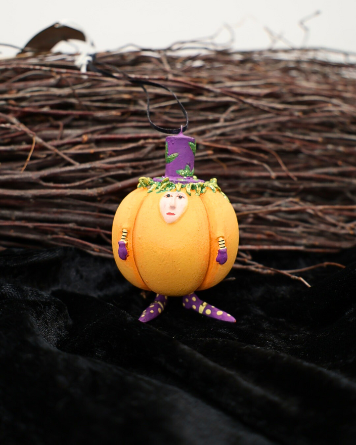 Vor einem Reisigbesen und auf einem schwarzen Samttuch dekorierter Krinkle Kürbis Mini Gourdon von Patience Brewster.