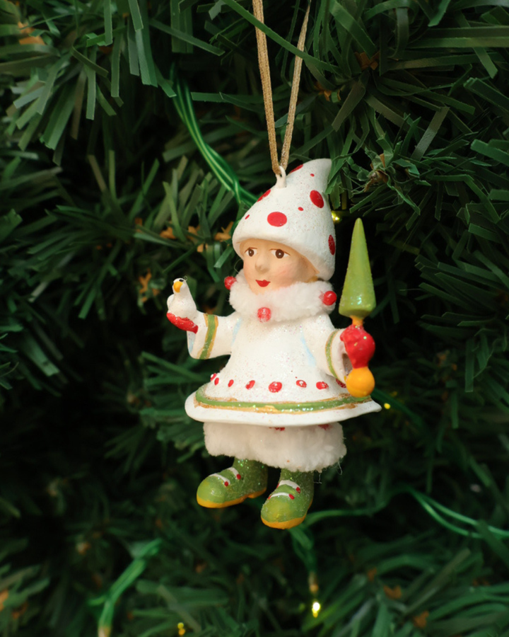 Mini "Blitzens Elf" Krinkles hängt an einem Tannenbaum. Zu sehen ist ein größtenteils weiß bekleideter Elf mit roten Pünktchen. In den Händen hält es jeweils einen kleinen Vogel und ein kleinen Tannenbaum Stab.