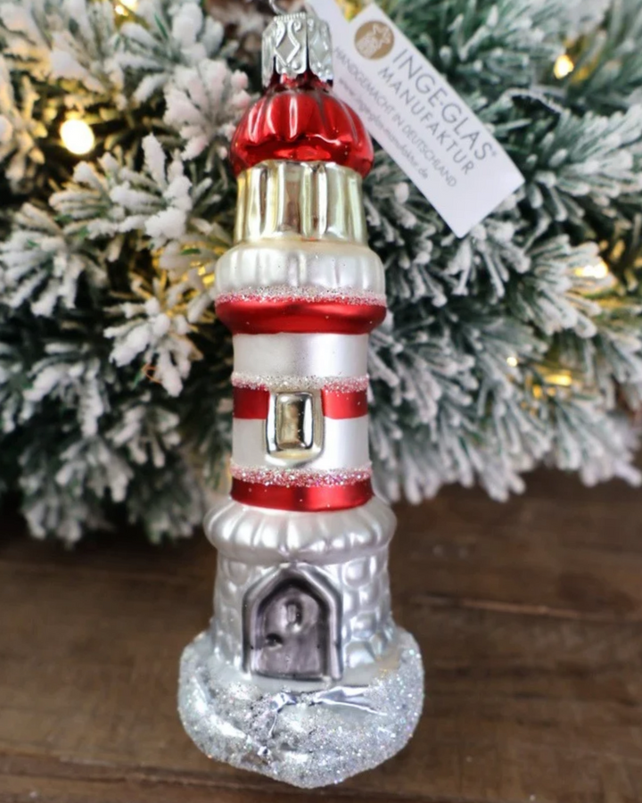 Weihnachtliches Leuchtturm Ornament von Inge Glas dekoriert vor weiß gepudertem Tannengrün auf einem Holztisch.
