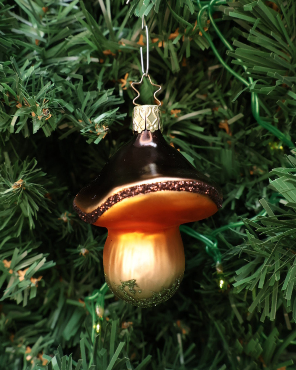 In einem Tannenbaum hängendes Pilz Ornament "Marone" von Inge Glas zum Aufhängen. In Deutschland handgefertigter Pilzanhänger aus Glas mit weißlichem Pilzstiel, orange-brauner Pilzhutunterseite und einem dunkelbraunen Pilzhut.