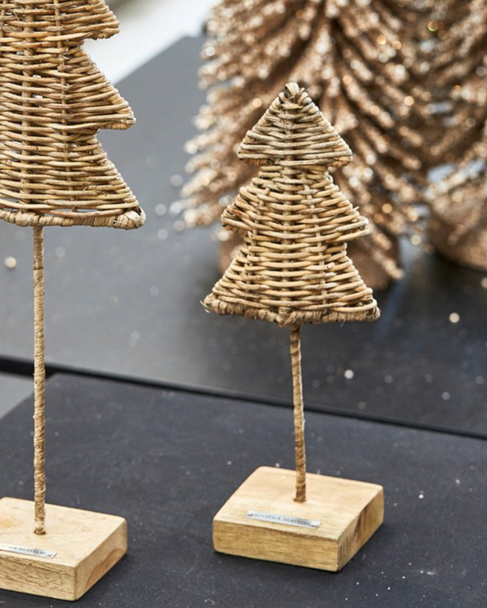 Weihnachtsdekoration mit Rustic Rattan Weihnachtsbaum „Christmas Tree“ von Rivièra Maison auf einem schwarzen Tisch.