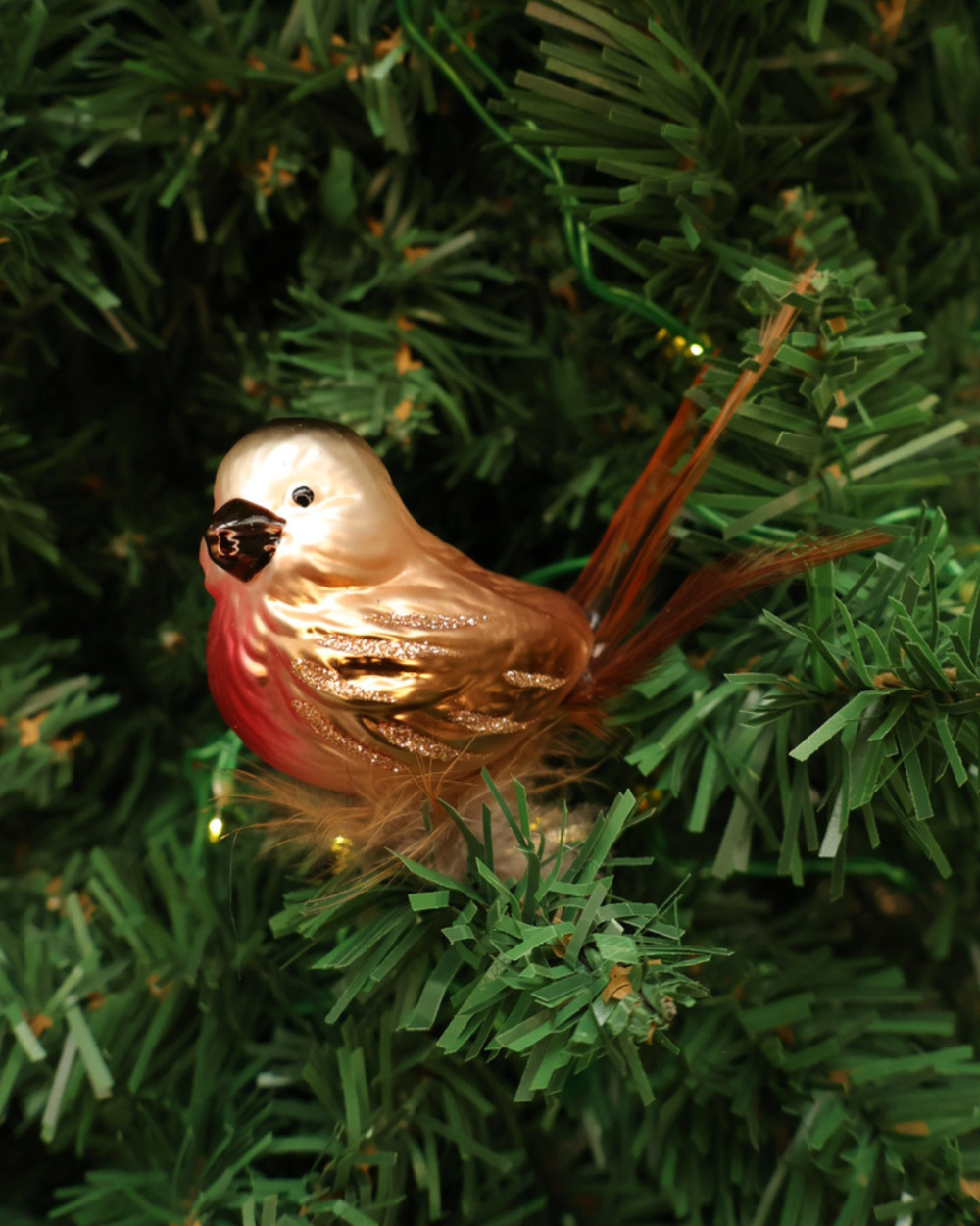 Dekorierter Vogel Weihnachtsbaumschmuck "Rotkehlchen" zum Klemmen hängt an Tannenbaum. Zu sehen ist ein Bronze Rotkehlchen mit einem roten Hals und bronze Federn welcher in die Kamera schaut.