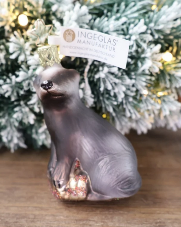 Weihnachtliches Dachs Ornament von Inge Glas dekoriert vor weiß gepudertem Tannengrün auf einem Holztisch.