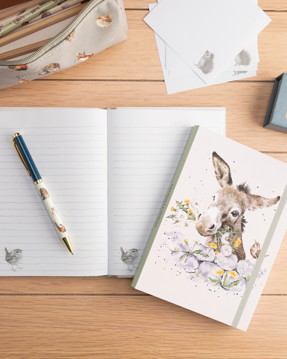 Dekorierte Szene mit offenem Esel Flexi-Notizbuch B6 „Fine and Dandy“ von Wrendale Designs auf hellem Holztisch, kombiniert mit Stift, Karten und Mäppchen.