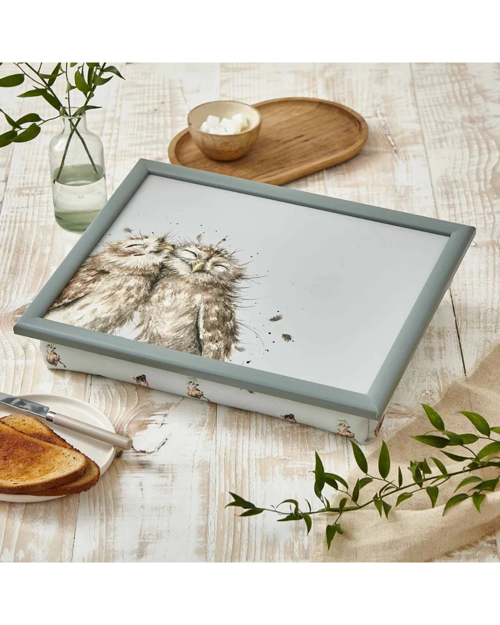 Knietablett „Owl“ auf Holztisch mit Toast & Pflanzen im Hintergrund