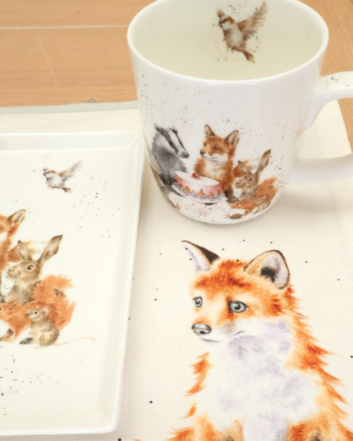 Dekoriertes Tischset, Teller und Tasse Woodland-Party von Wrendale Designs auf einem Holztisch.