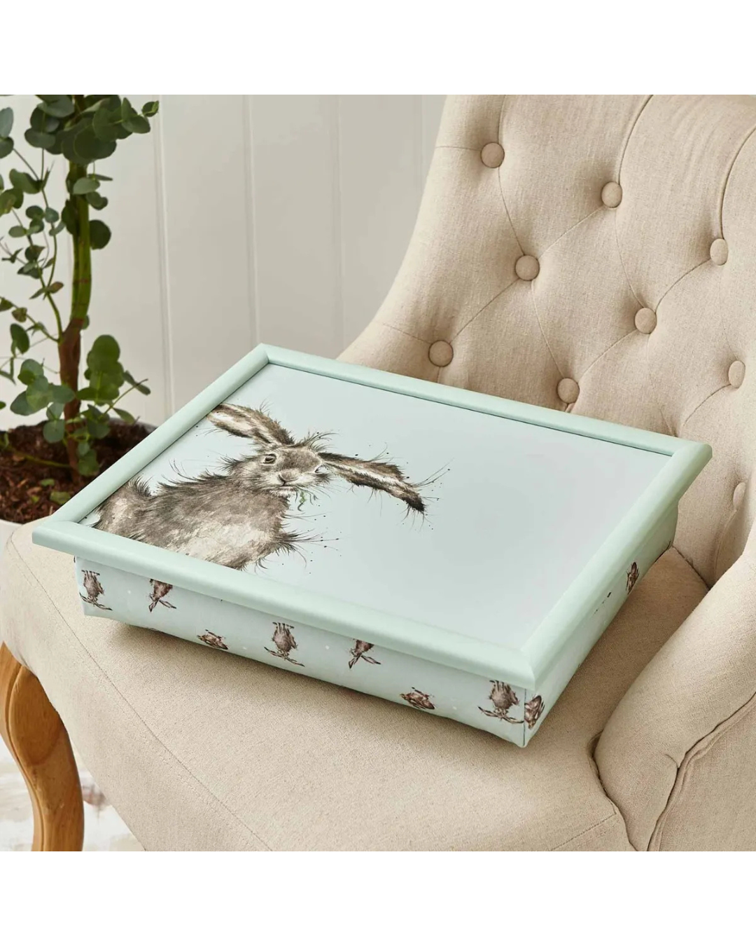 Knietablett „Hare“ auf beigefarbenem Sessel mit Pflanze im Hintergrund