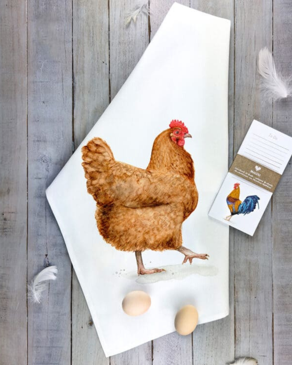 Hennen Geschirrtuch Catwalk Chicken von Maluu dekorativ auf Holzfläche mit Eiern und Produktanhänger drapiert