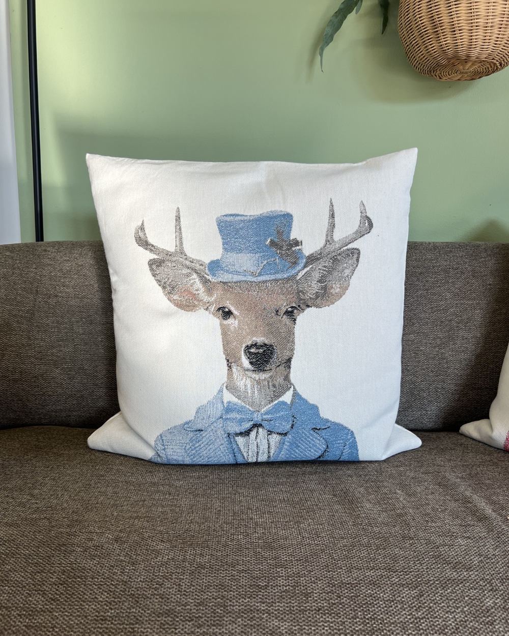 Hirschkissen "Dandy" von Sander in blauem Anzug mittig auf einer braunen Couch stehend. Das Hirschmotiv ist gut zu erkennen.