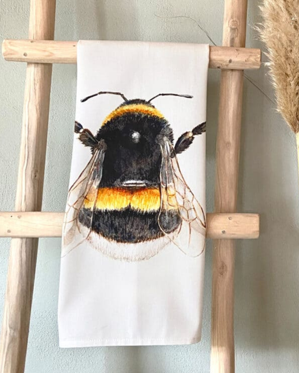 Hummel Geschirrtuch „Bumble Bee“ von Maluu dekorativ auf Holzleiter drapiert mit sichtbarem Hummelmotiv in Schwarz-Gelb