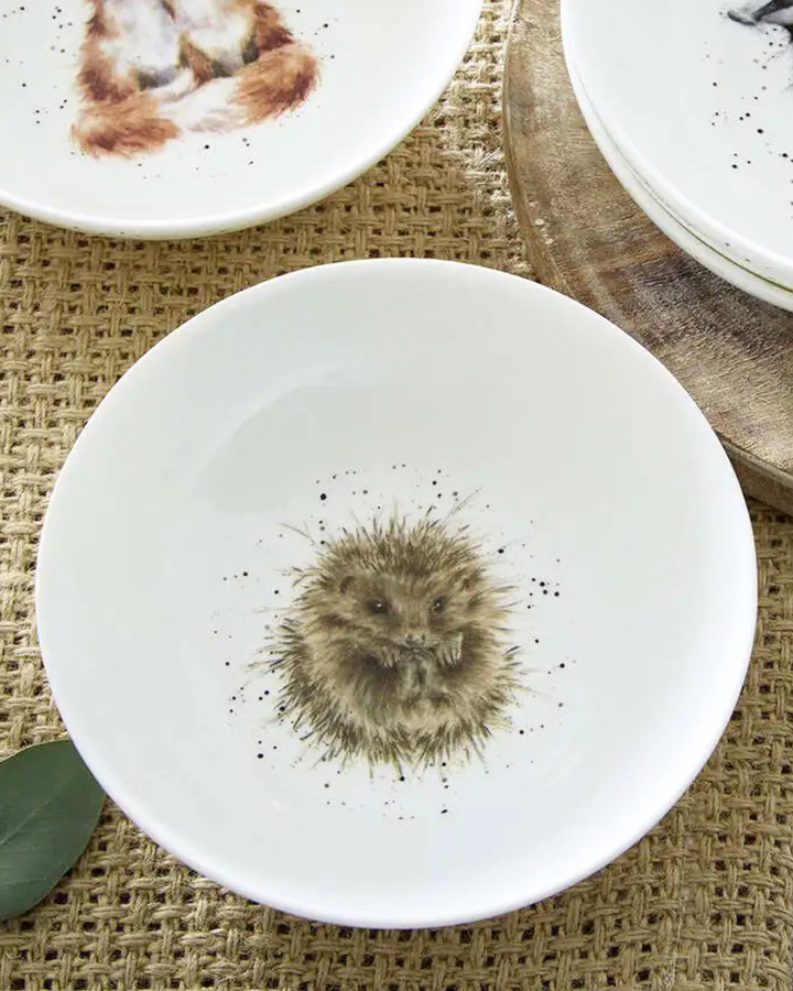Weißes Igel Schüsselchen "Royal Worchester" aus Porzellan von Wrendale Designs auf einem gedeckten Tisch. Das Motiv zeigt einen eingerollten Igel welcher in die Kamera schaut. Auf dem Tisch sind andere Schüsselchen im selben Stil erkennbar.