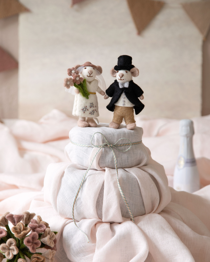 Abgebildet ist das Hochzeitspaar Maus als Filzanhänger von Gry & Sif in Weiß mit weißer Jacke und im schwarzen Anzug mit Hut. auf einem rosa Tuch.