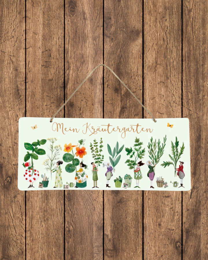 Metallschild „Kräutergarten“ vom Grätz Verlag an einer Holzwand aufgehängt, mit illustrierten Kräutern, kleinen Figuren und Schriftzug „Mein Kräutergarten“, befestigt mit Kordel.