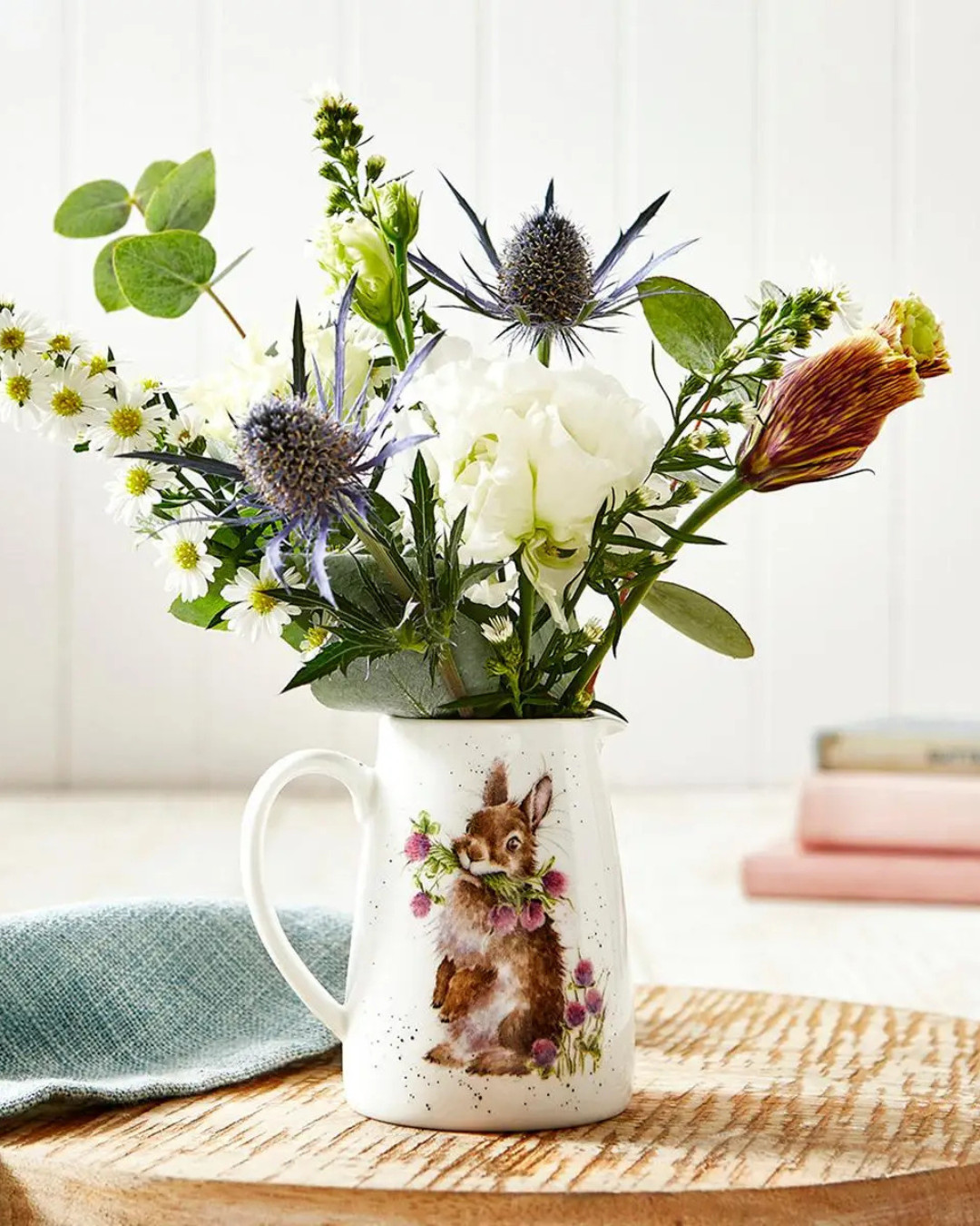 Hasen Krug von Wrendale Designs gefüllt mit Blumen Auf einem runden Holztisch im Wohnzimmer. Das Motiv des Krugs ist ein niedlicher Hase welcher Blumen mit den Zähnen hält.
