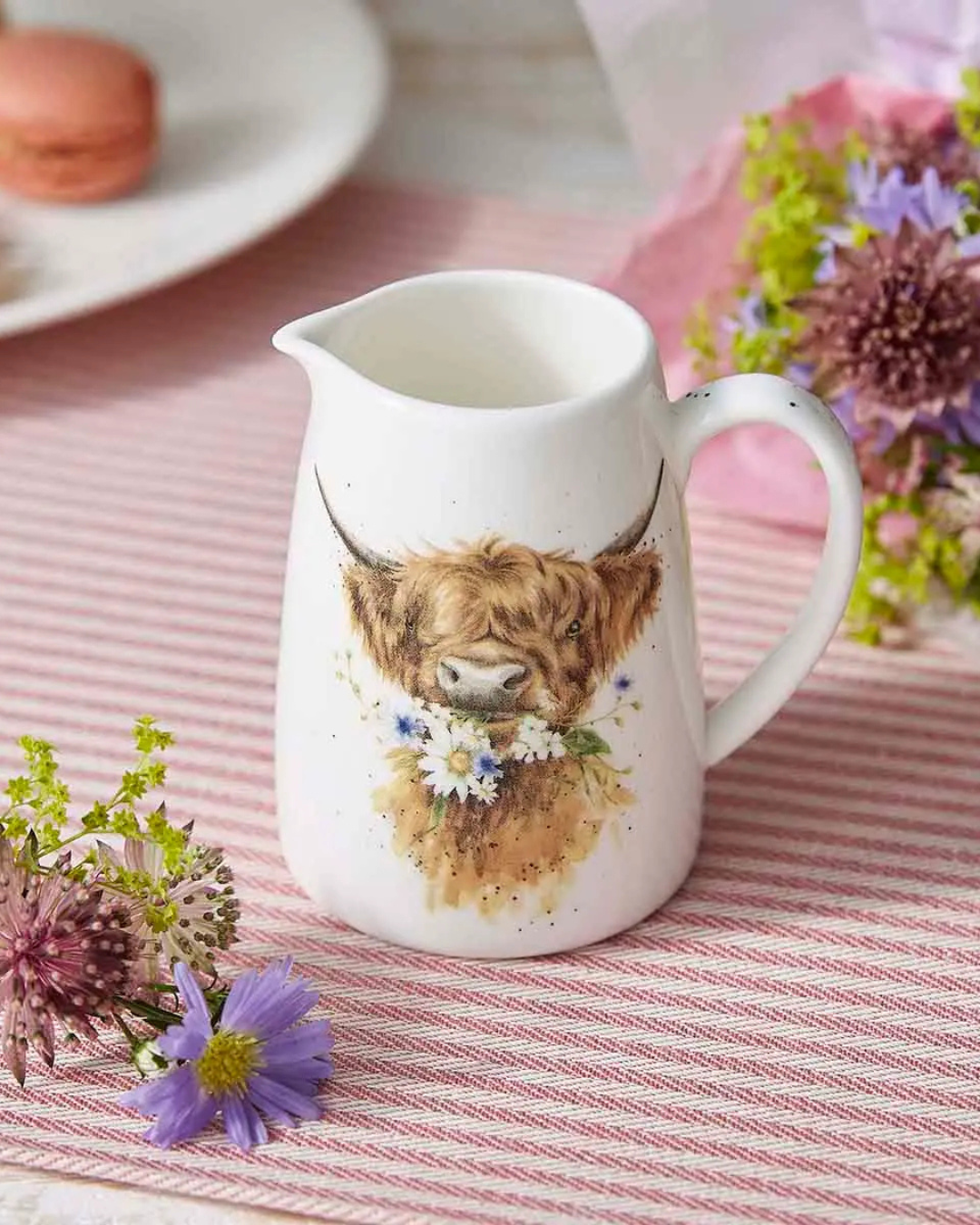 Seitlich oben fotografierter Mini Krug mit Hochlandkuh Motiv welcher auf einem pink gedeckten und mit pinken Blumen dekorierten Tisch steht.