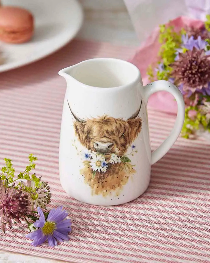 Seitlich oben fotografierter Mini Krug mit Hochlandkuh Motiv welcher auf einem pink gedeckten und mit pinken Blumen dekorierten Tisch steht.