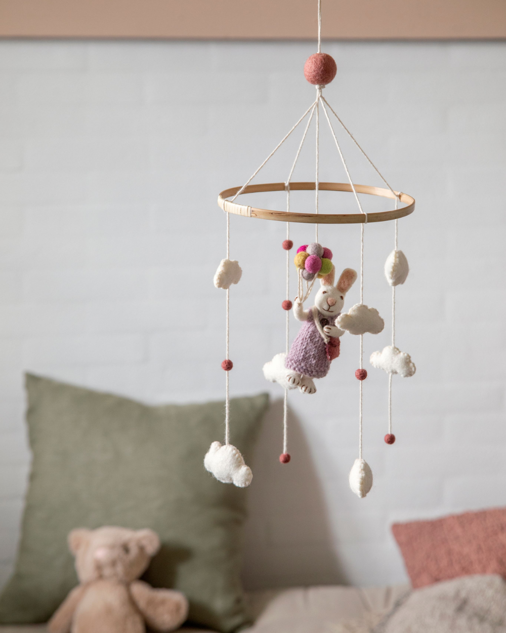 Filz-Mobile von Gry & Sif hängt frei im Raum vor einer hellen Wand, im Hintergrund sind ein Sofa, Kissen und ein Stofftier unscharf zu sehen, das Mobile steht ruhig im Vordergrund.