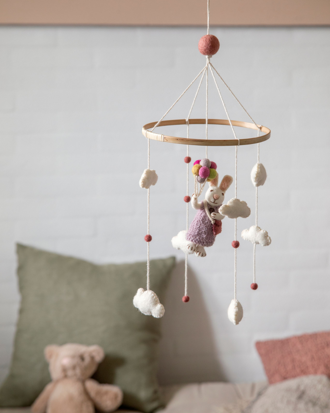 Filz-Mobile von Gry & Sif hängt frei im Raum vor einer hellen Wand, im Hintergrund sind ein Sofa, Kissen und ein Stofftier unscharf zu sehen, das Mobile steht ruhig im Vordergrund.