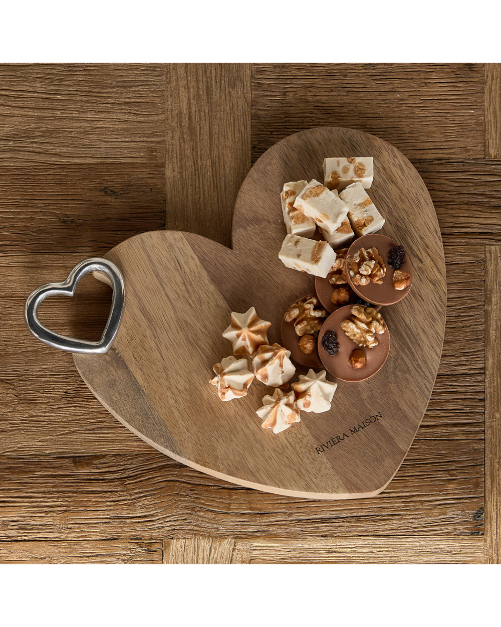 Dekorierte Szene mit dem Schneidebrett „Lovely Heart Chopping Board“ von Rivièra Maison in Herzform, belegt mit süßen Kleinigkeiten auf rustikalem Holztisch.