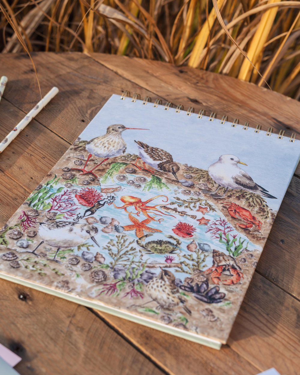 Wrendale Designs Skizzenbuch A4 Seaside mit Küstenmotiv auf Holztisch dekoriert mit Stift