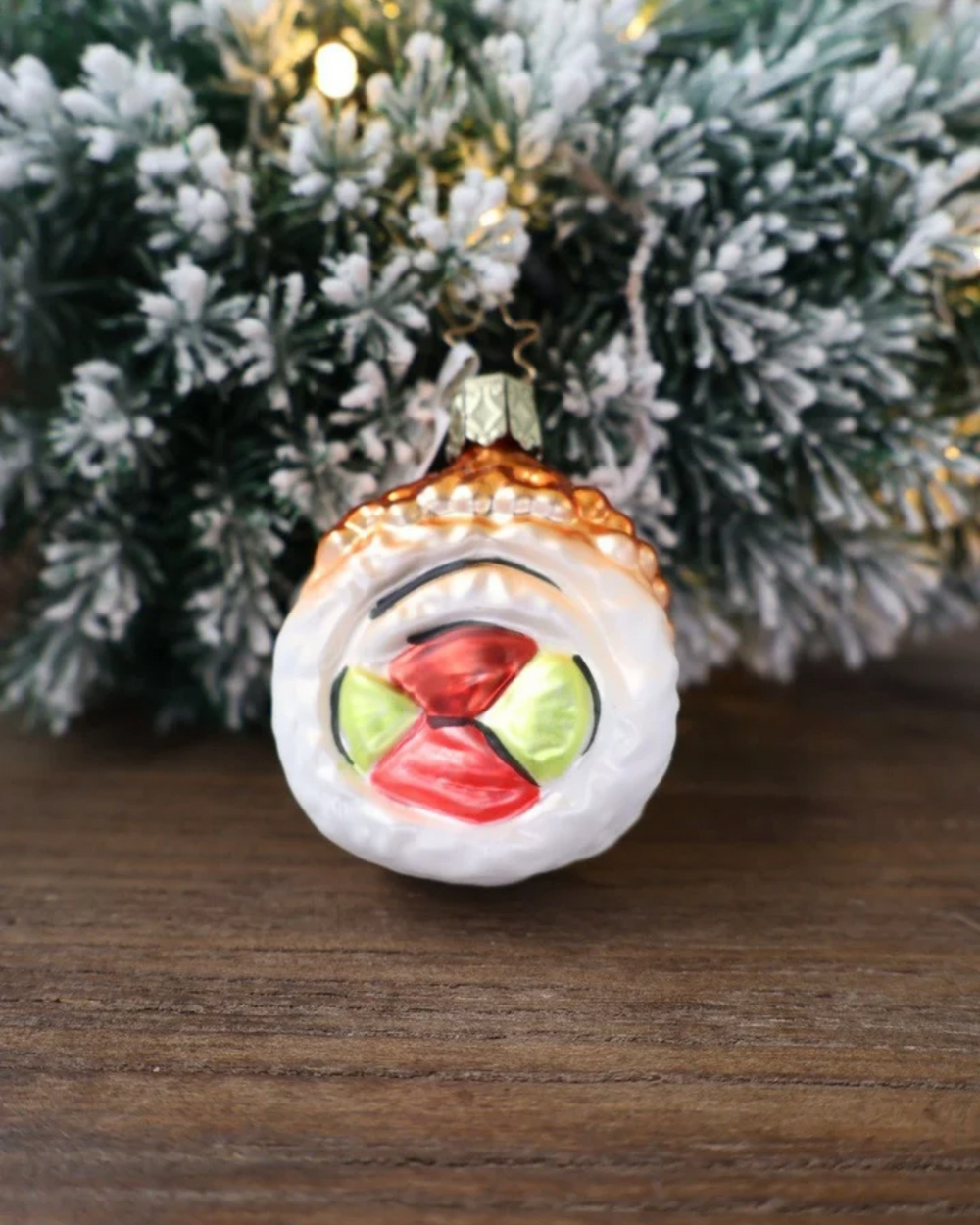 Weihnachtliches Sushi Ornament von Inge Glas dekoriert vor weiß gepudertem Tannengrün auf einem Holztisch.