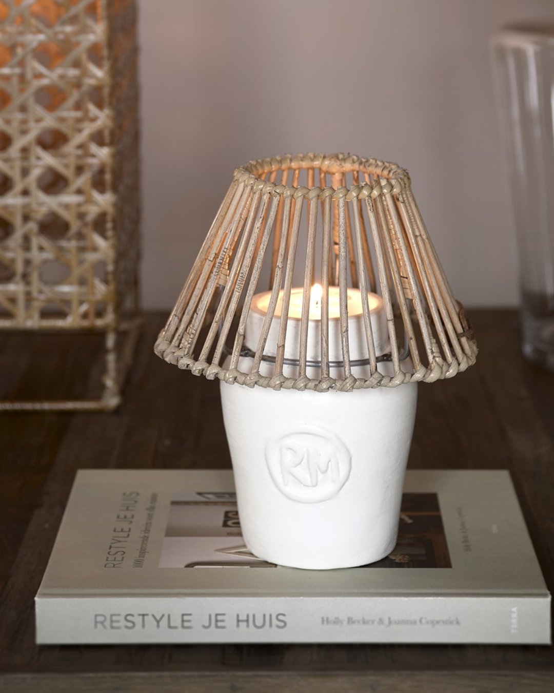 Windlicht „RM Clay Candle Holder“ von Rivièra Maison mit brennendem Teelicht auf einem Buch dekoriert.