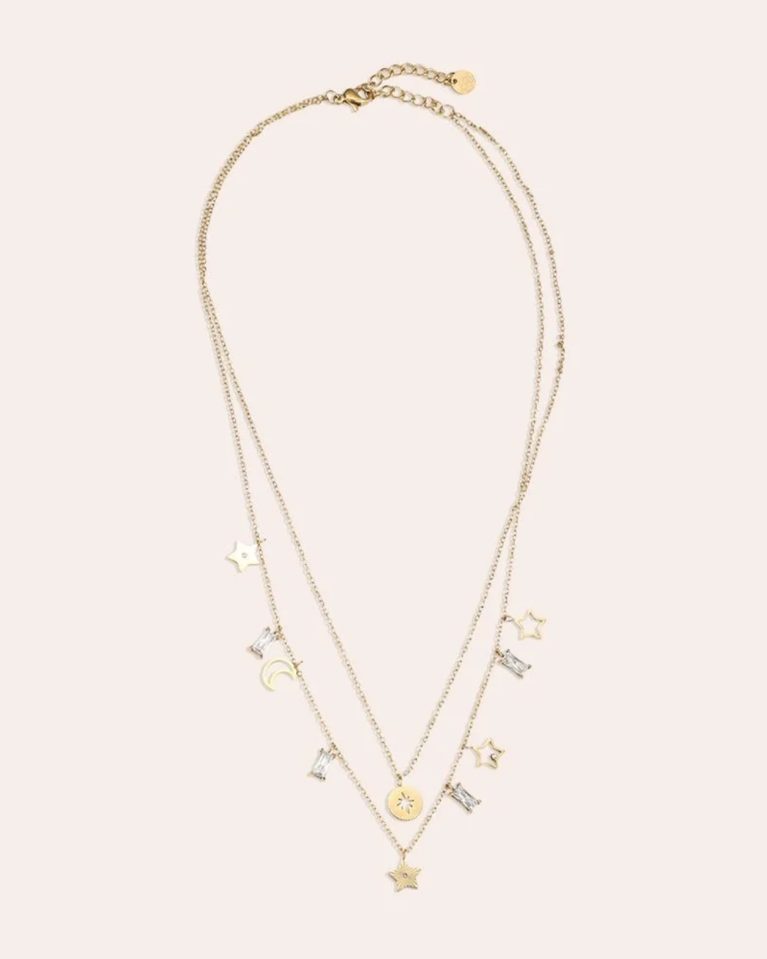 Doppellagige Kette mit Sternen und Mond von Dottilove in gold vor beigen Hintergrund. Die Kette ist größtenteils Gold mit Stern und Mond Anhängern und weißen Steinen.