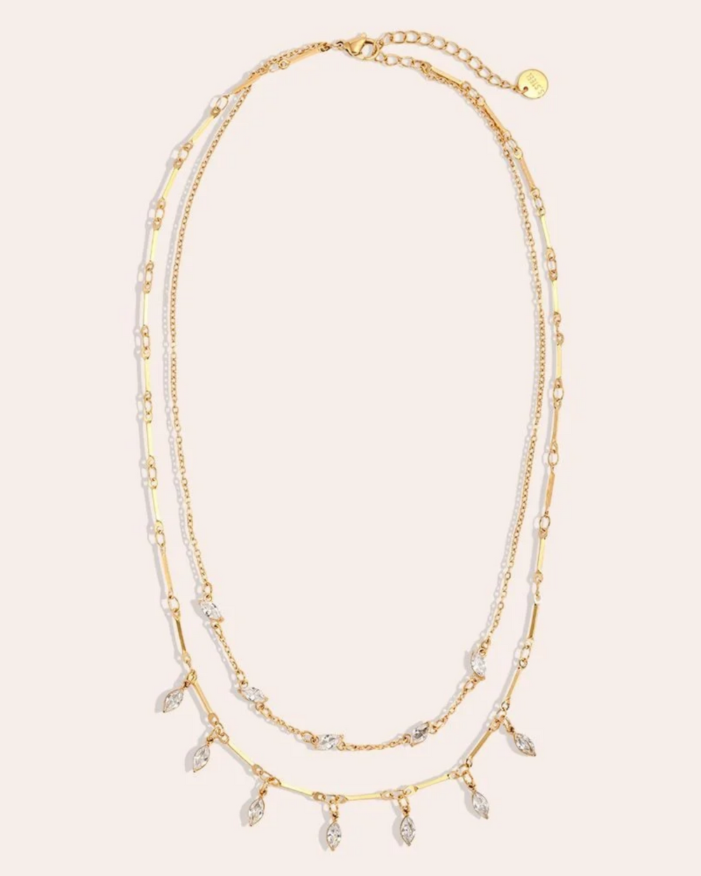 goldene Doppellagigen Kette von Dottilove mit weißen Steinen vor beigen Hintergrund. Die Kette ist größtenteils Gold mit weißen ovalen Steinen.