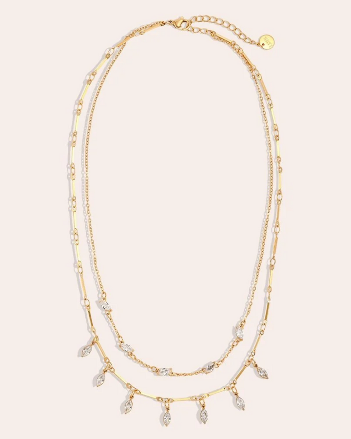 goldene Doppellagigen Kette von Dottilove mit weißen Steinen vor beigen Hintergrund. Die Kette ist größtenteils Gold mit weißen ovalen Steinen.