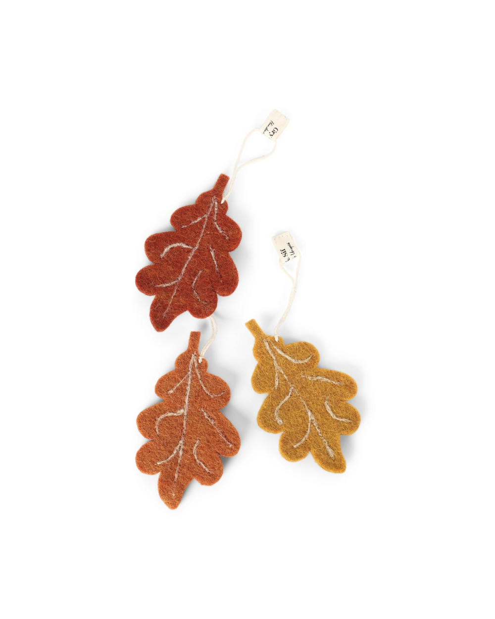 Drei herbstliche Filzanhänger in Eichenblatt-Form von Gry & Sif in Currygelb, Orange und Dunkelorange vor weißem Hintergund.