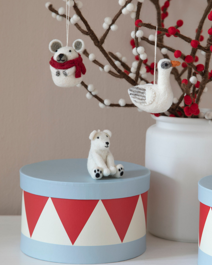 Filzanhänger "sitzender Eisbär" von Gray & Sif aus handgefertigtem weißen Filz. Der Eisbär sitzt auf einer blau, rot, weißen Dose und über ihm hängen eine Maus und eine Gans aus Filz von Filzzweigen mit weißen und roten Beeren herab.