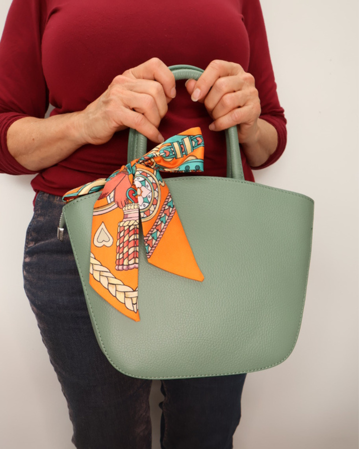 Seegrüne Handtasche aus Leder Lotte vom Südstrand mit orangenem Bandana frontal getragen vor weißen Hintergrund.