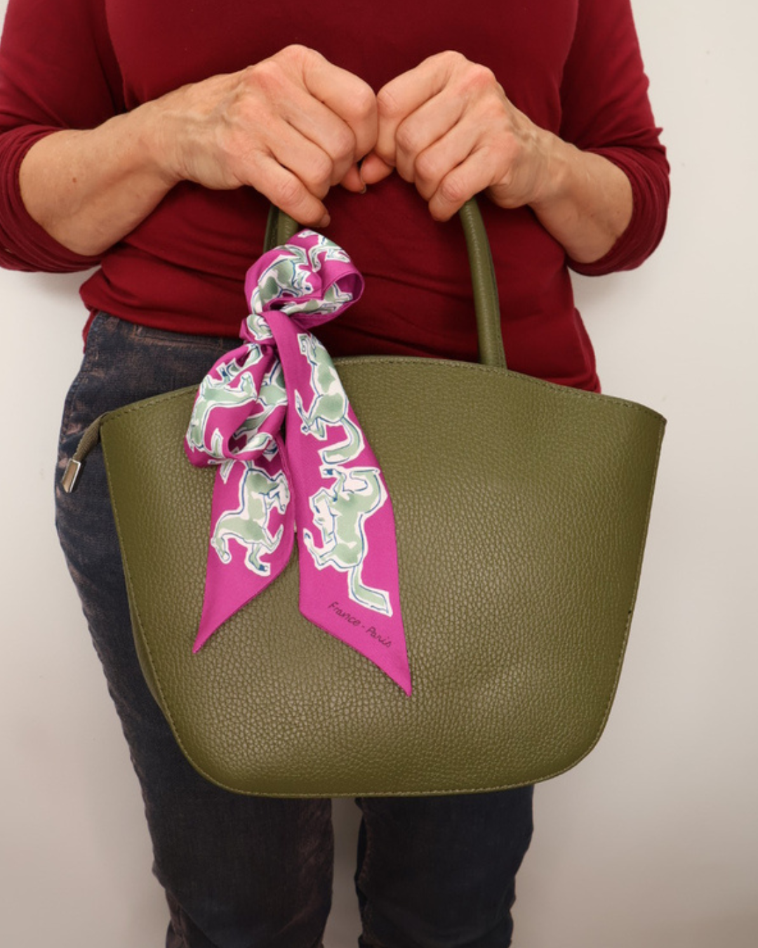 Waldgrüne Handtasche aus Leder Lotte vom Südstrand mit pinken Bandana frontal getragen vor weißen Hintergrund.
