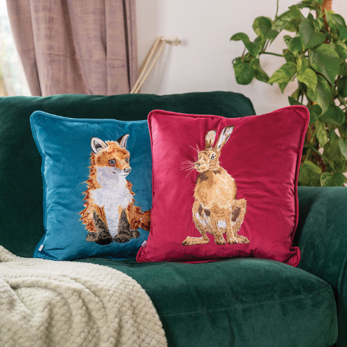 Kombination des petrolfarbenen Fuchs Kissens mit dem weinroten Hasen Kissens von Wrendale Designs auf einer dunkelgrünen Couch.