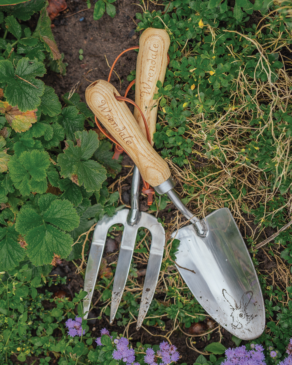 Fork & Trowel Gartenwerkzeug von Wrendale Designs im Beet zwischen Gras und Blüten liegend