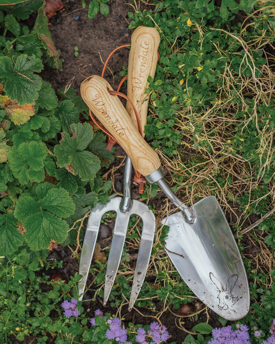 Fork & Trowel Gartenwerkzeug von Wrendale Designs im Beet zwischen Gras und Blüten liegend