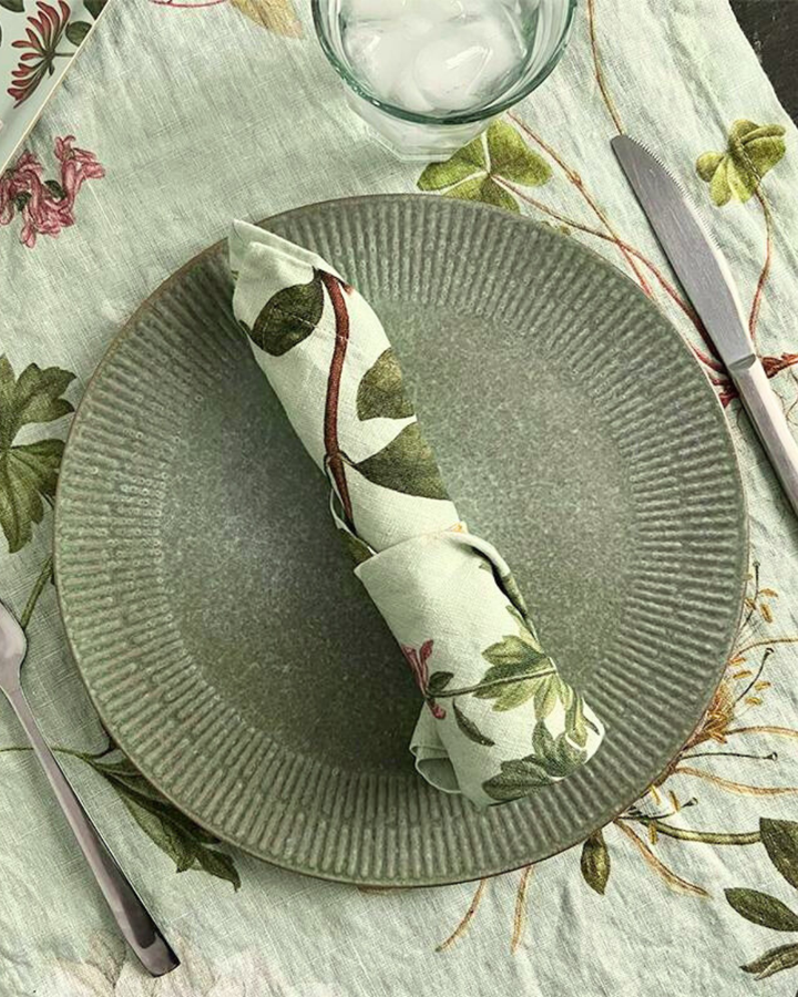Leinenserviette "Flora Danica Atlas" von Koustrup & Co., locker gefaltet neben Gabel auf Tischdecke mit botanischen Motiven.