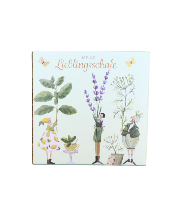 Verpackung der Müslischale „Kräutergarten“ vom Grätz Verlag mit dem Aufdruck „Meine Lieblingsschale“ und Illustrationen von drei Figuren mit verschiedenen Kräutern und Schmetterlingen.