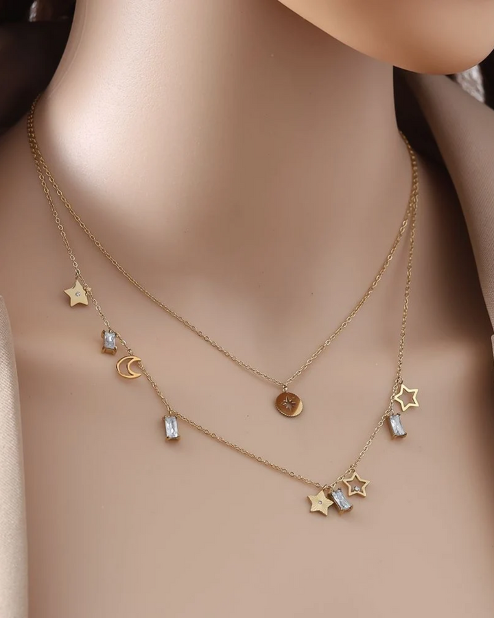 von einer Puppe getragene Doppellagige Kette mit Sternen und Mond von Dottilove in gold. Die Kette ist größtenteils Gold mit Stern und Mond Anhängern und weißen Steinen.