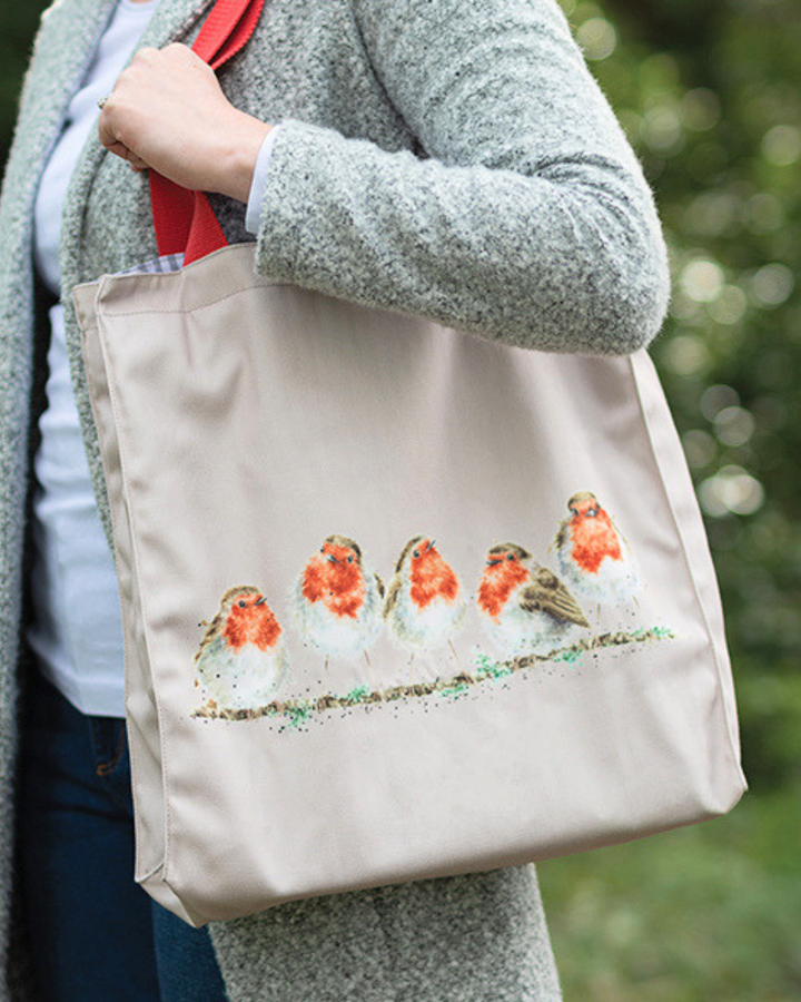 Rotkehlchen Einkaufstasche von Wrendale Designs. Zu sehen ist eine Frau mit blauer Jeans, weißem Oberteil und einem grauen Mantel welche die Hellgraue Rotkehlchen Tasche um ihre Schulter trägt.