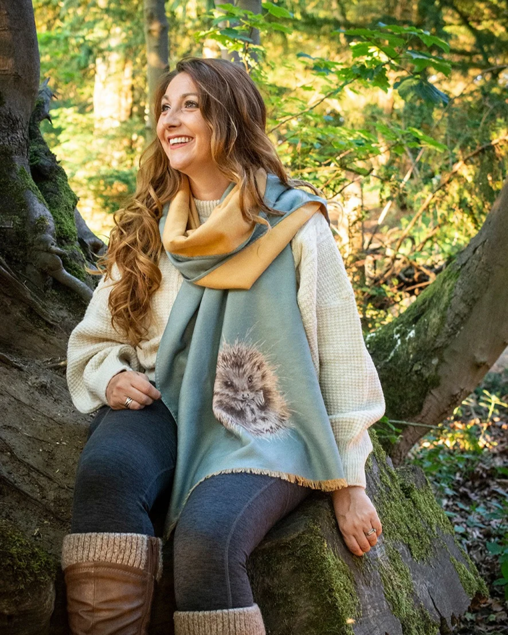 Von einer Frau getragener Igel Schal "Awakening" von Wrendale Designs sitzen auf einem Baum in einem Wald. die Gelbe Rückseite des Schals ist gut erkennbar.