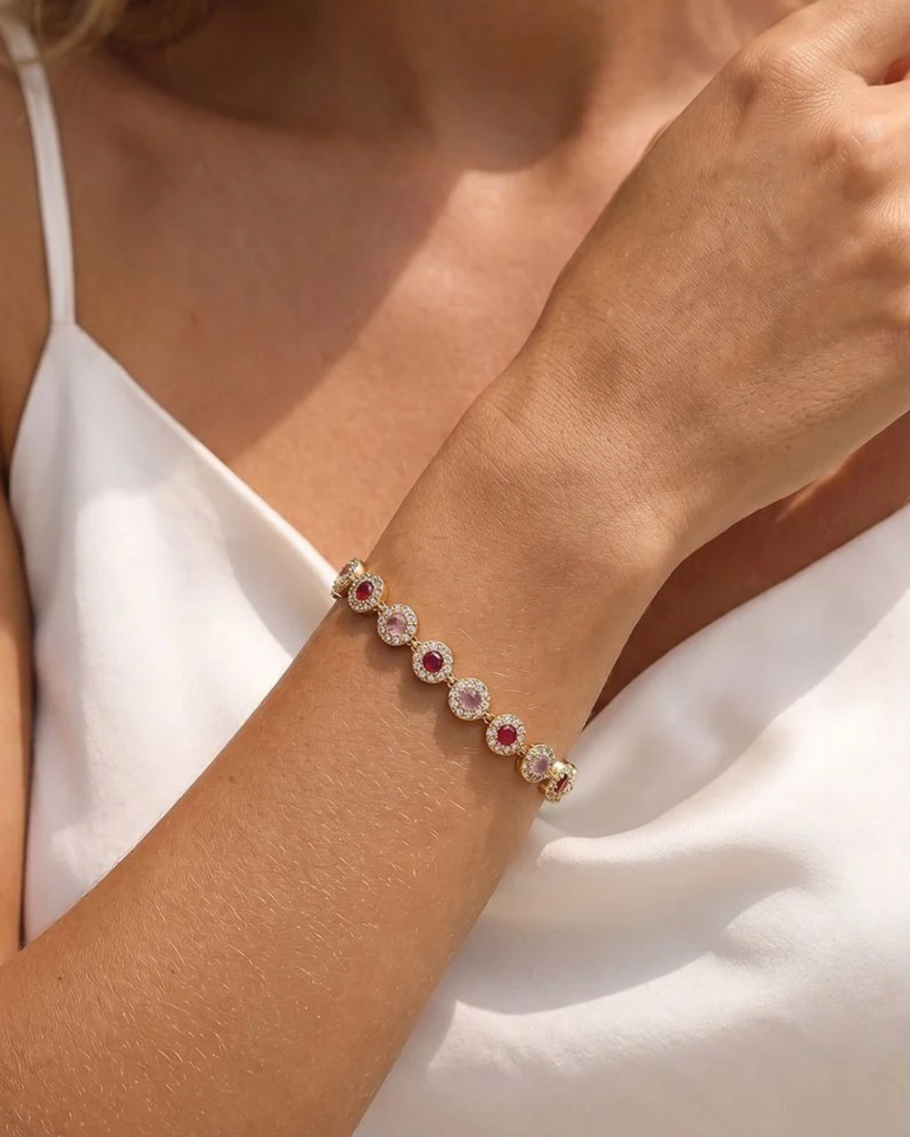 Nahaufnahme vom Armband mit bunten Glitzer Steinen von Dottilove getragen von einer Frau mit weißen Oberteil. Das Armband selbst ist Gold mit vielen Glitzer Steinen in rot, weiß und lila.